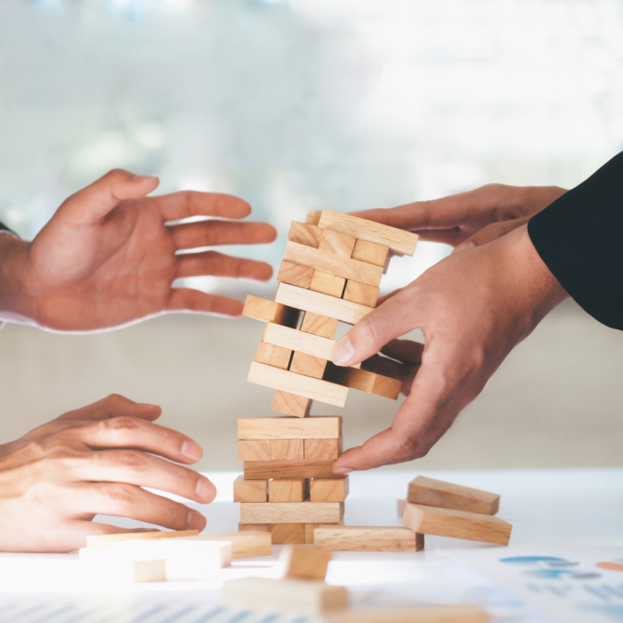 Risk Management Training Picture of two hands playing Jenga to represent risk in a business and how risk management simulations and risk management training helps.